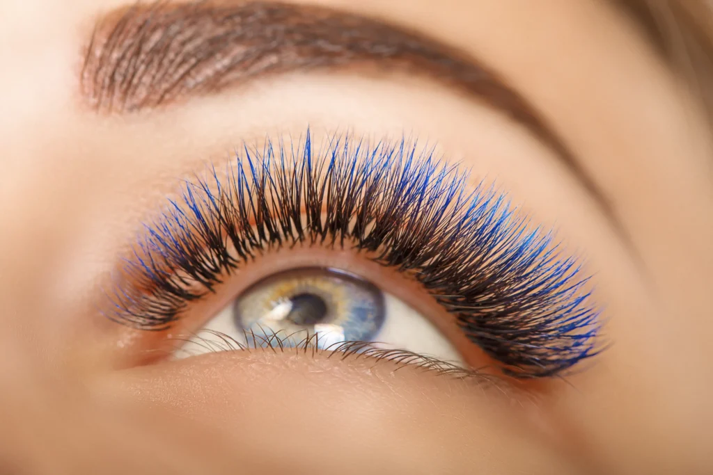 Close-up of a person's eye with long, thick eyelashes featuring blue highlights and a well-groomed eyebrow, showcasing the artistry of Lakeland Lash & Brow Studio.